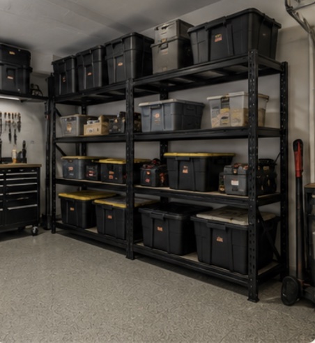 Black steel shelving racks filled with labelled storage
                     totes along a garage wall.