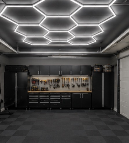 A garage with a hexagonal LED ceiling grid, tiled floor,
                     black cabinetry and a full tool wall.